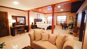 A spacious bedroom with a large bed, a sitting area with a sofa, a desk, and a television.