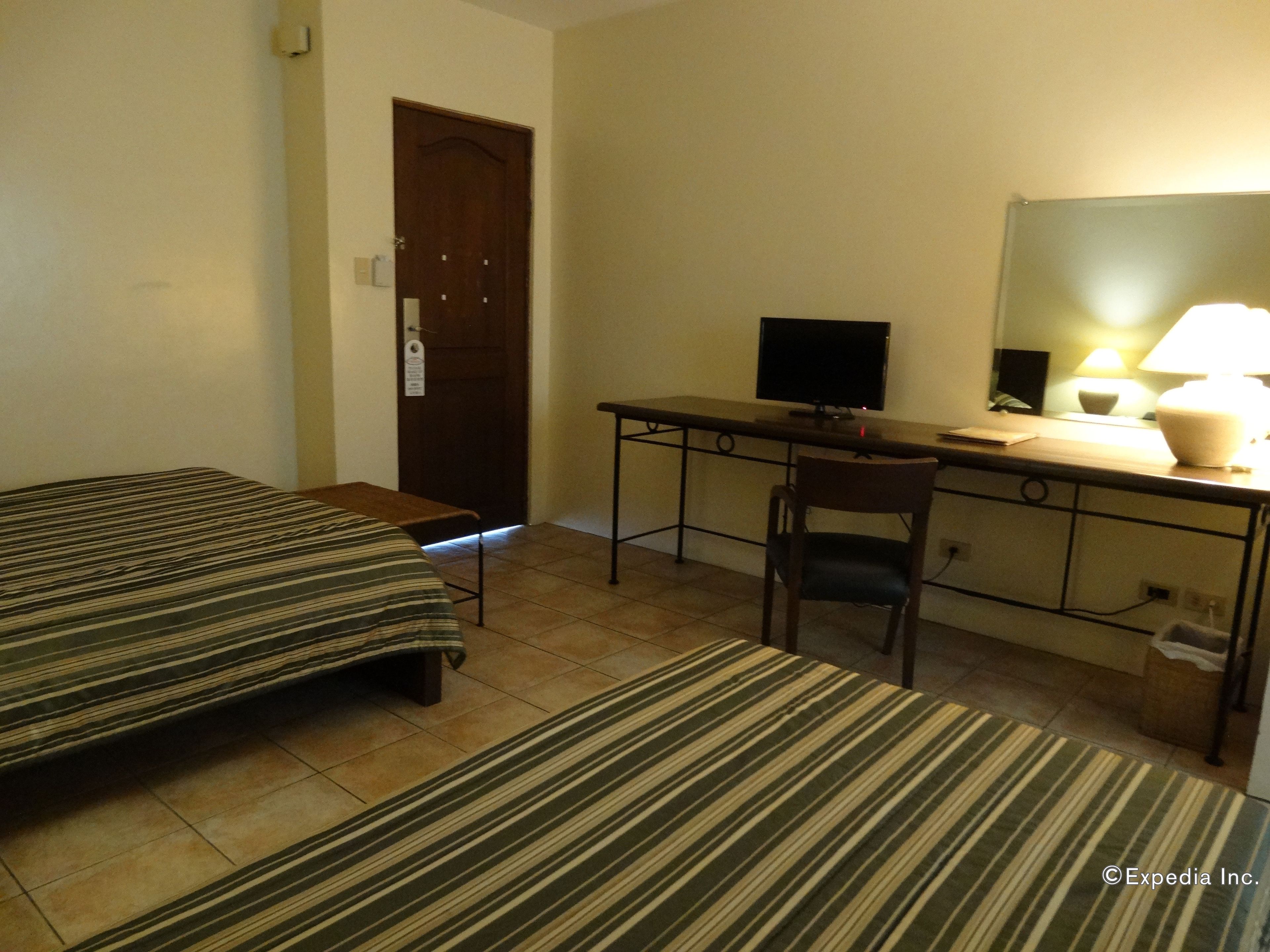 A hotel room with two single beds, a desk with a computer, a chair, a lamp, and a door.