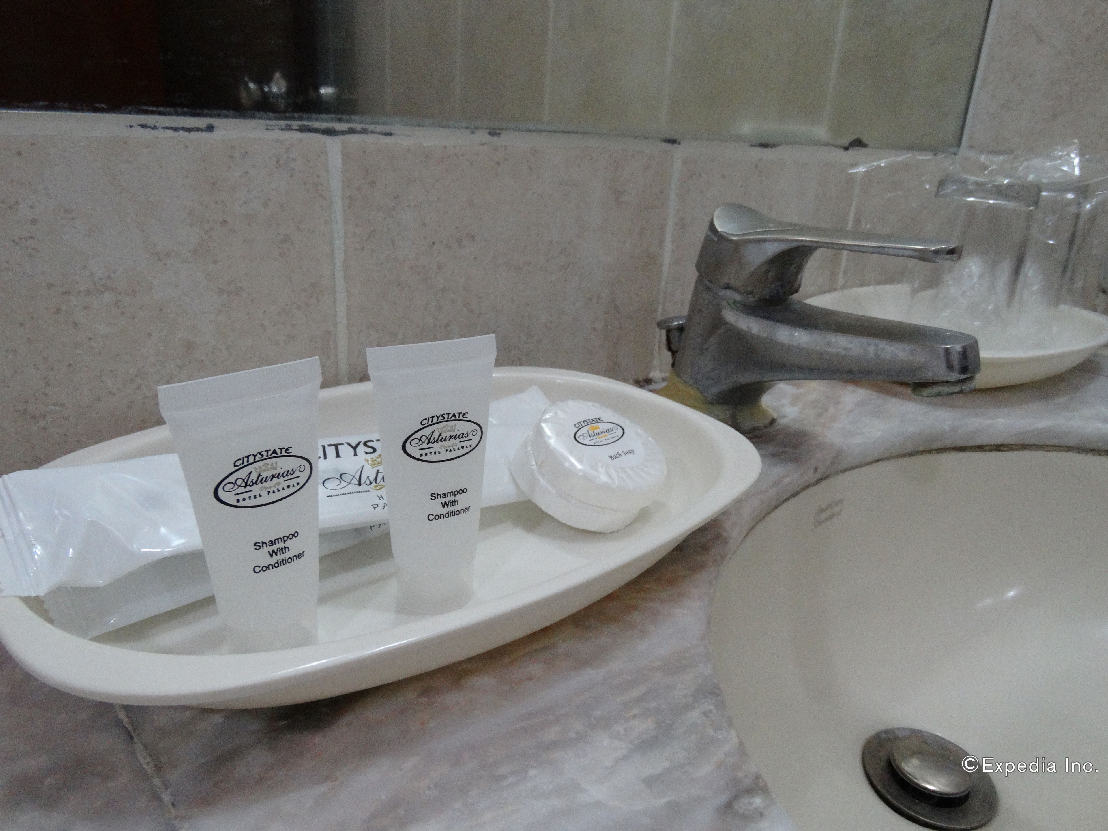 Un lavamanos de baño con artículos de aseo, incluyendo champú, acondicionador y jabón de baño.