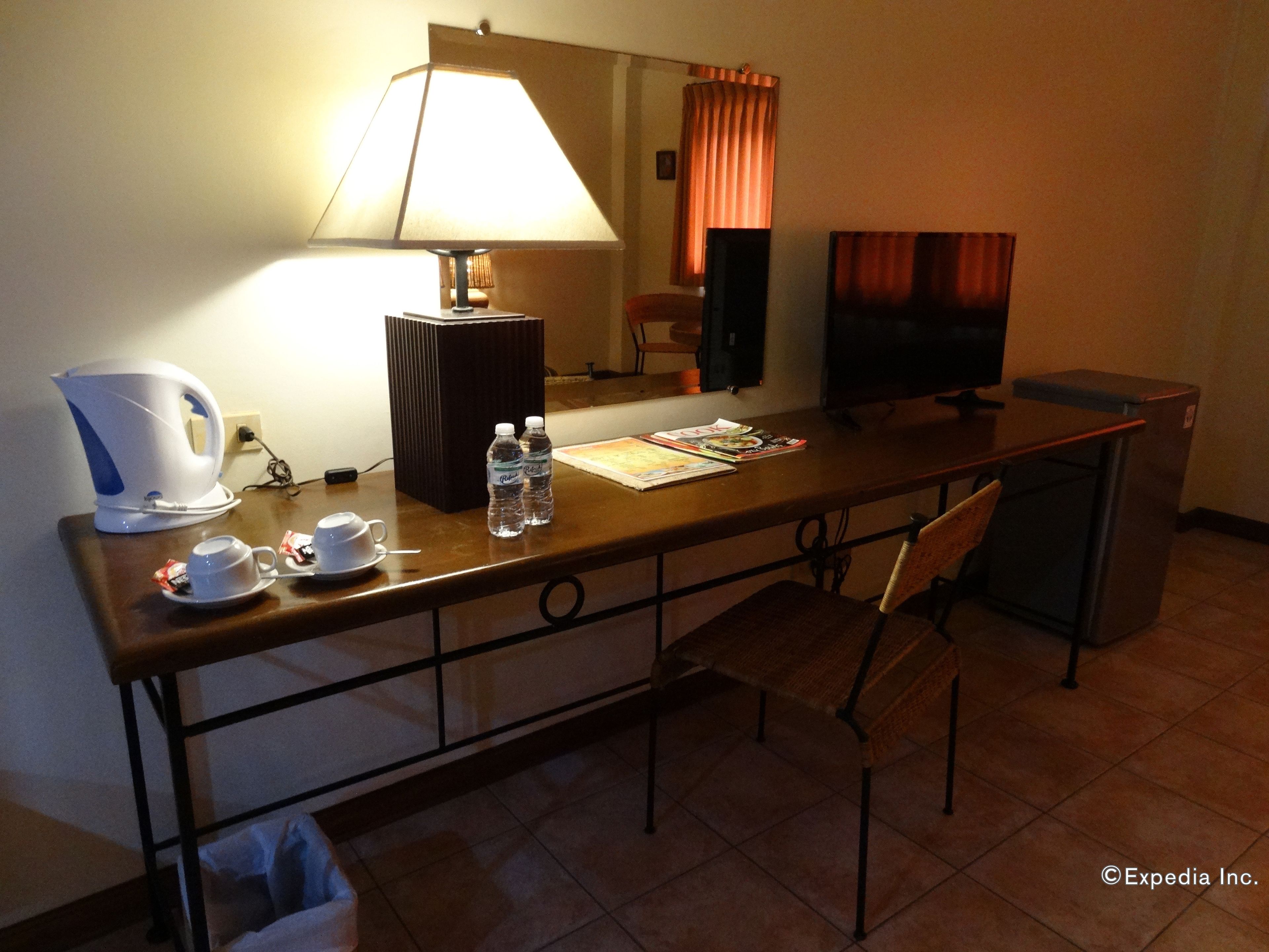 Una habitación de hotel con escritorio, lámpara, televisión, silla y cafetera.