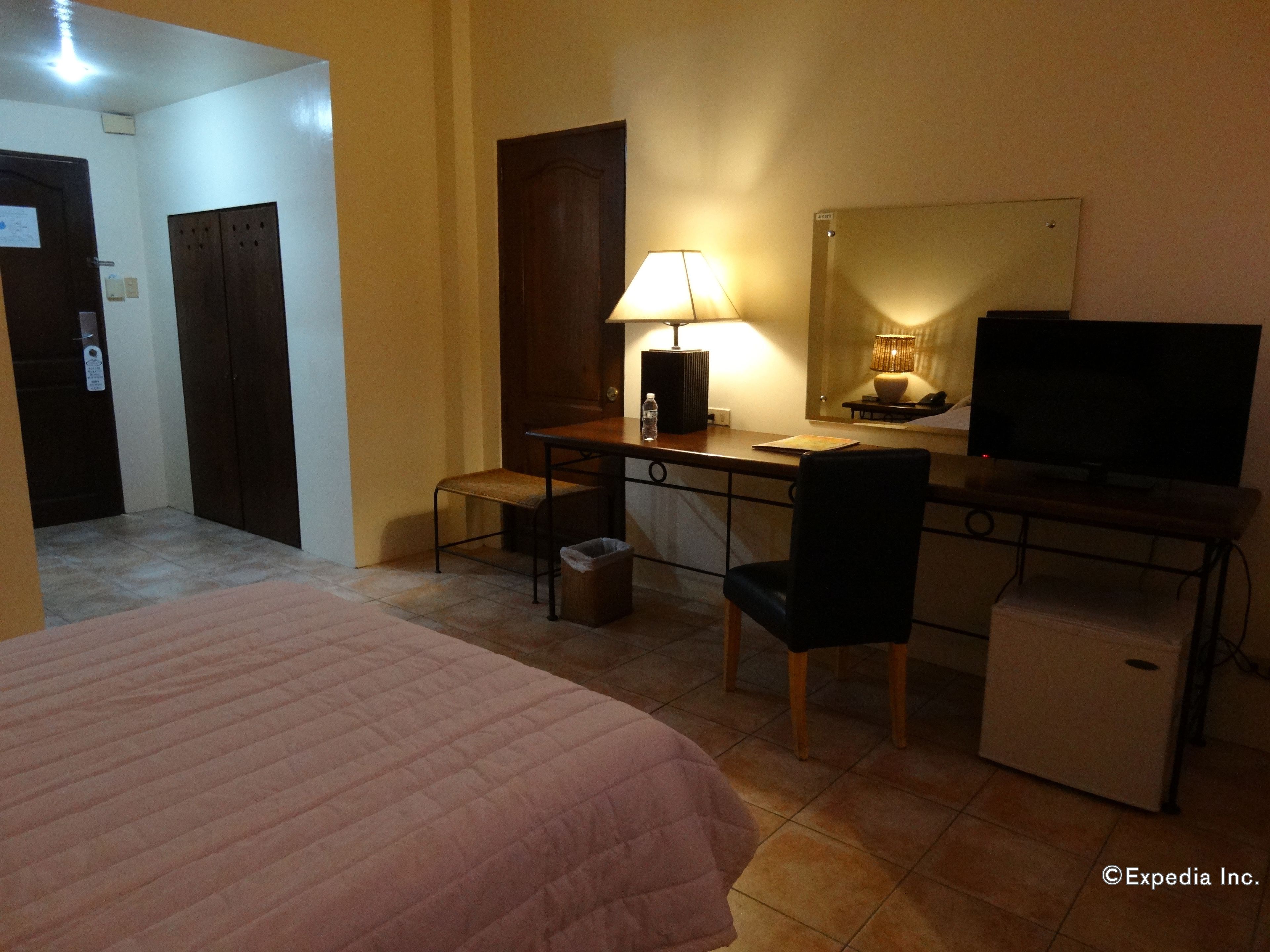 A hotel room with a bed, desk, chair, lamp, television, and a small refrigerator.
