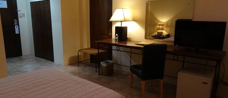 A hotel room with a bed, desk, chair, lamp, television, and a small refrigerator.