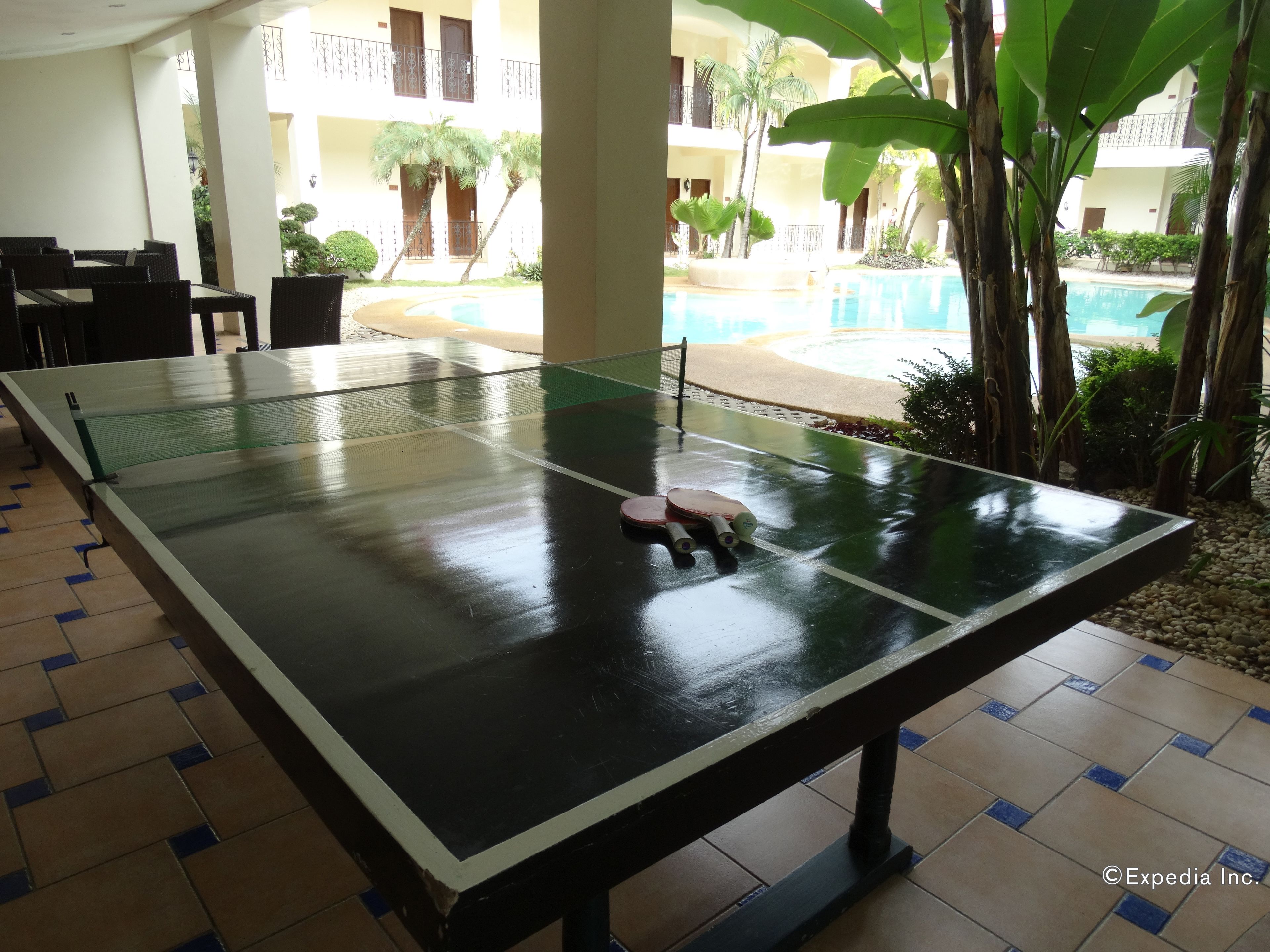 Une table de ping-pong dans la cour d’un hôtel, avec une piscine et des palmiers.