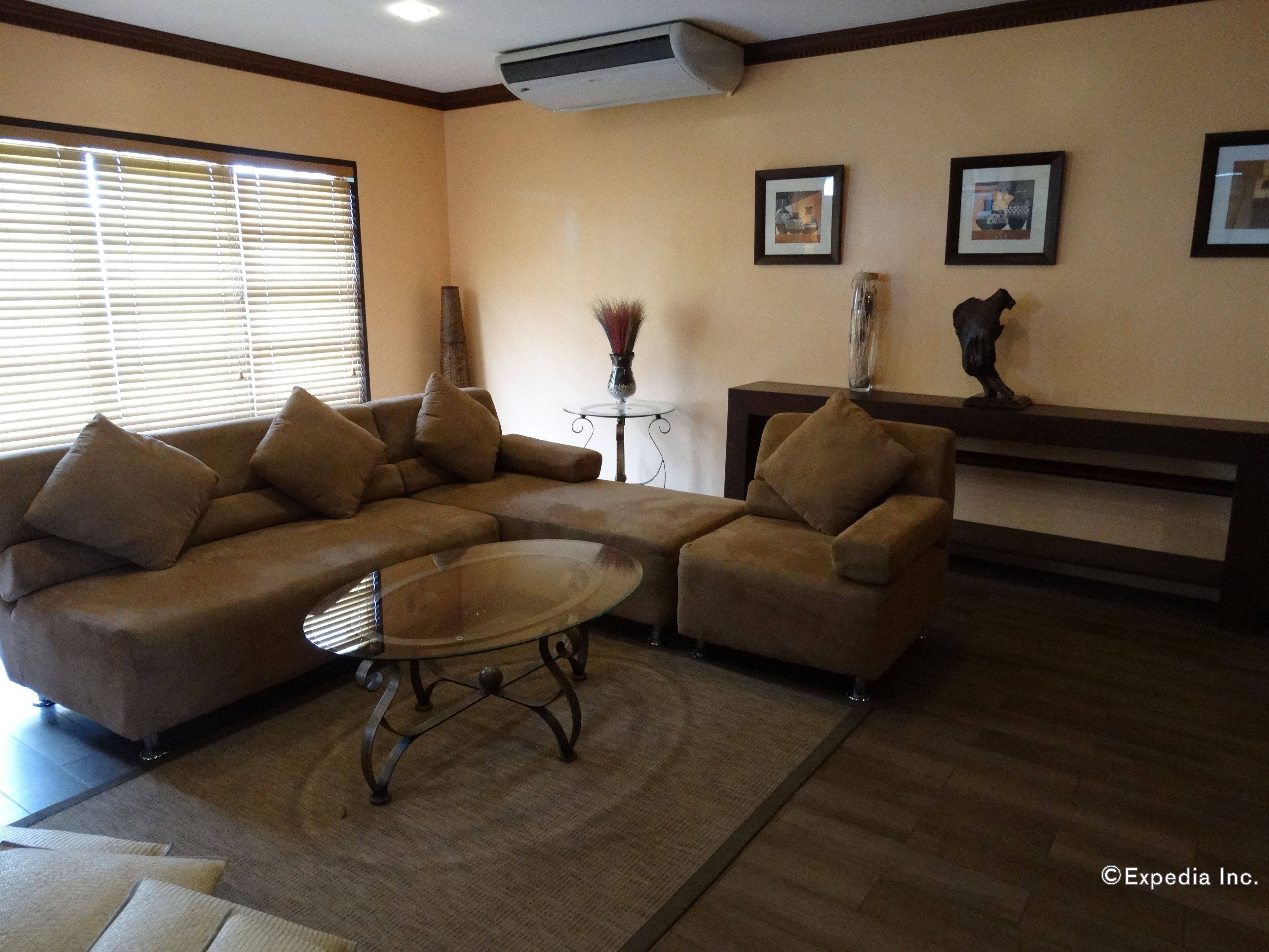 A living room with a sectional sofa, a coffee table, and a small side table. There are framed pictures on the wall and a statue on a console table.