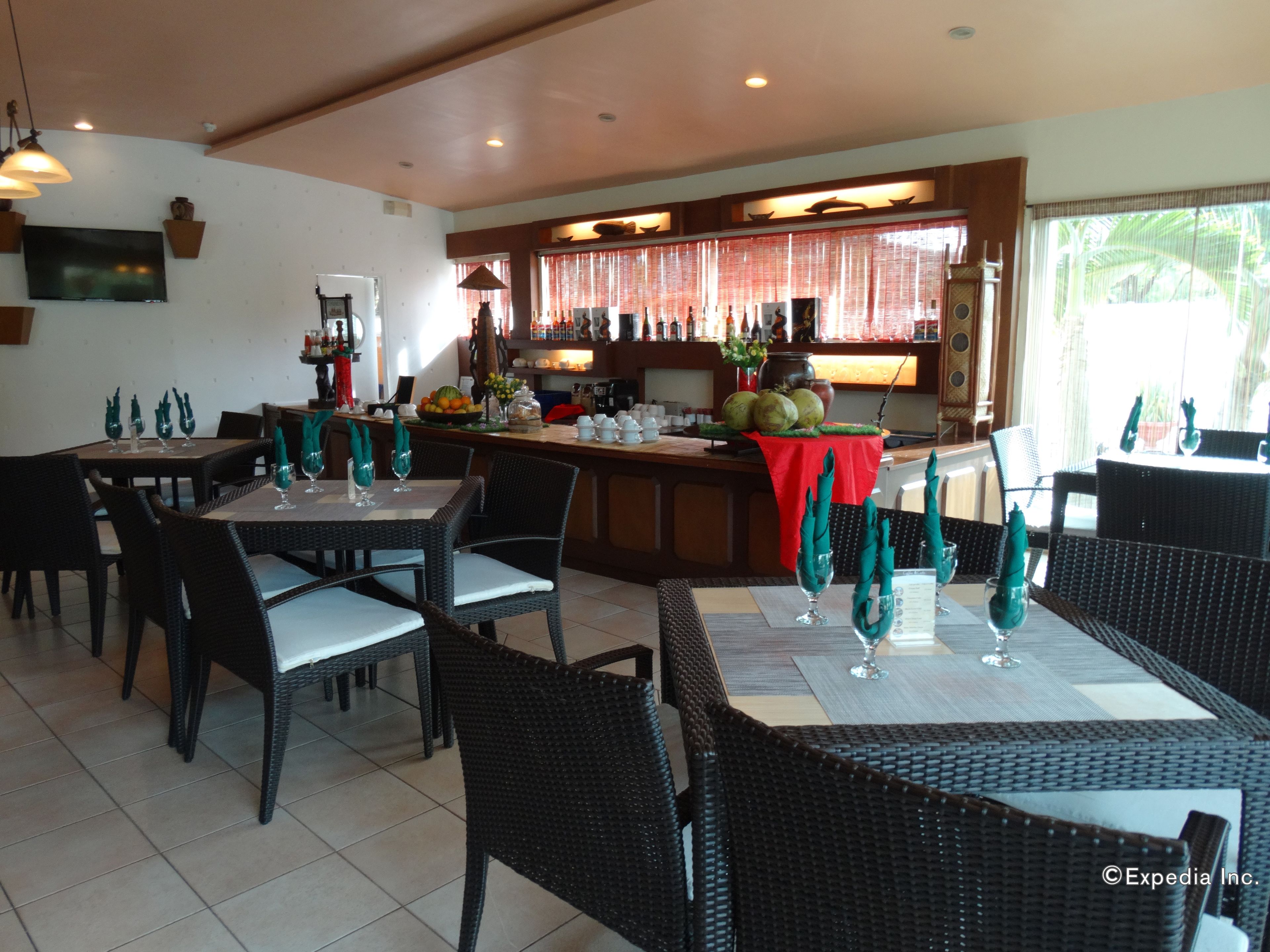 Een restaurant met een bar, eettafels met stoelen en een keuken op de achtergrond.