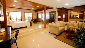 A hotel room with a bed, a sofa, a coffee table, and a dining area with a table and chairs.