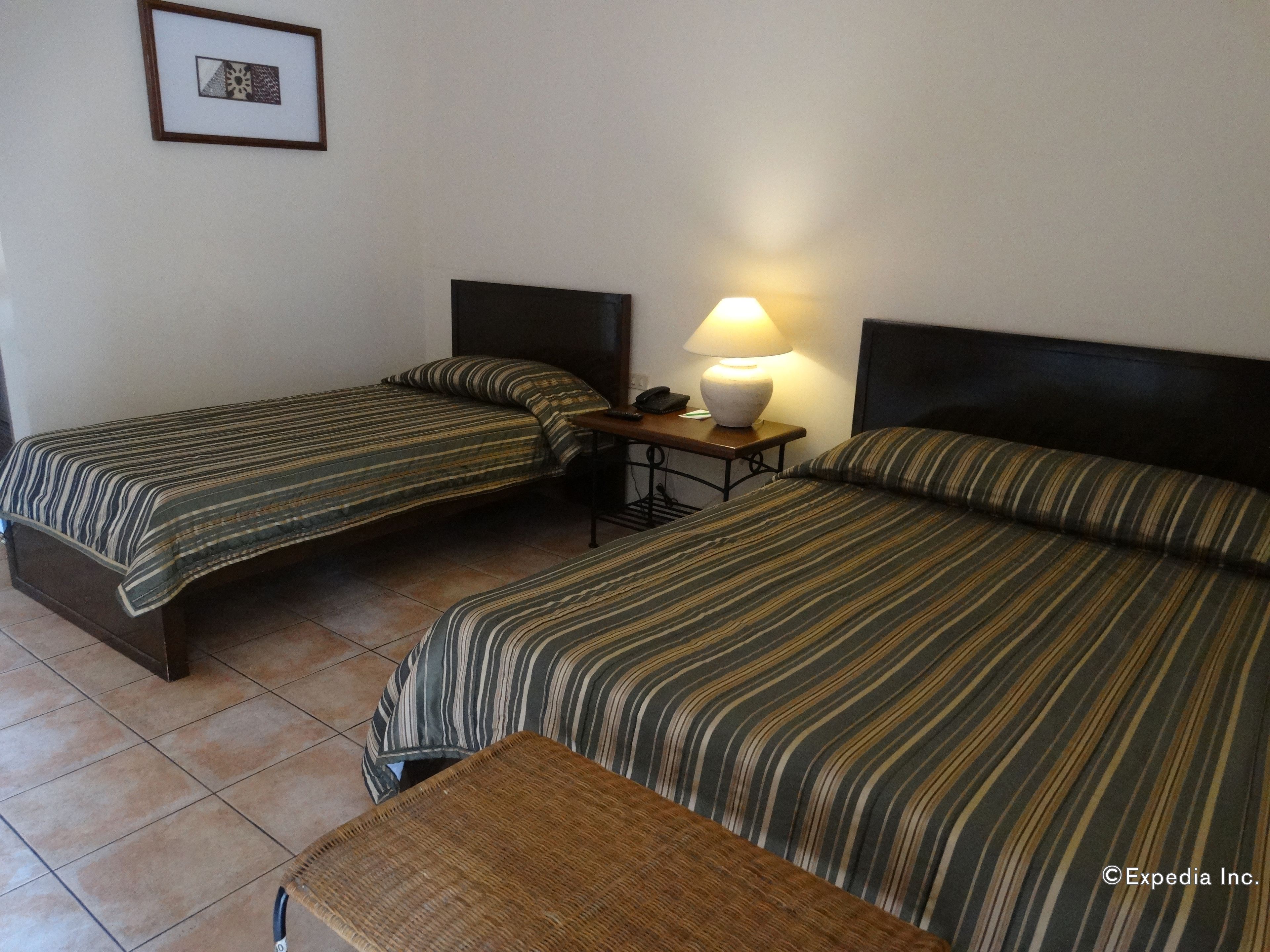 A hotel room with two single beds, a nightstand with a lamp, and a small bench.