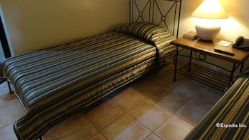 A single bed with a striped bedspread, a bedside table with a lamp, a book, and a telephone.