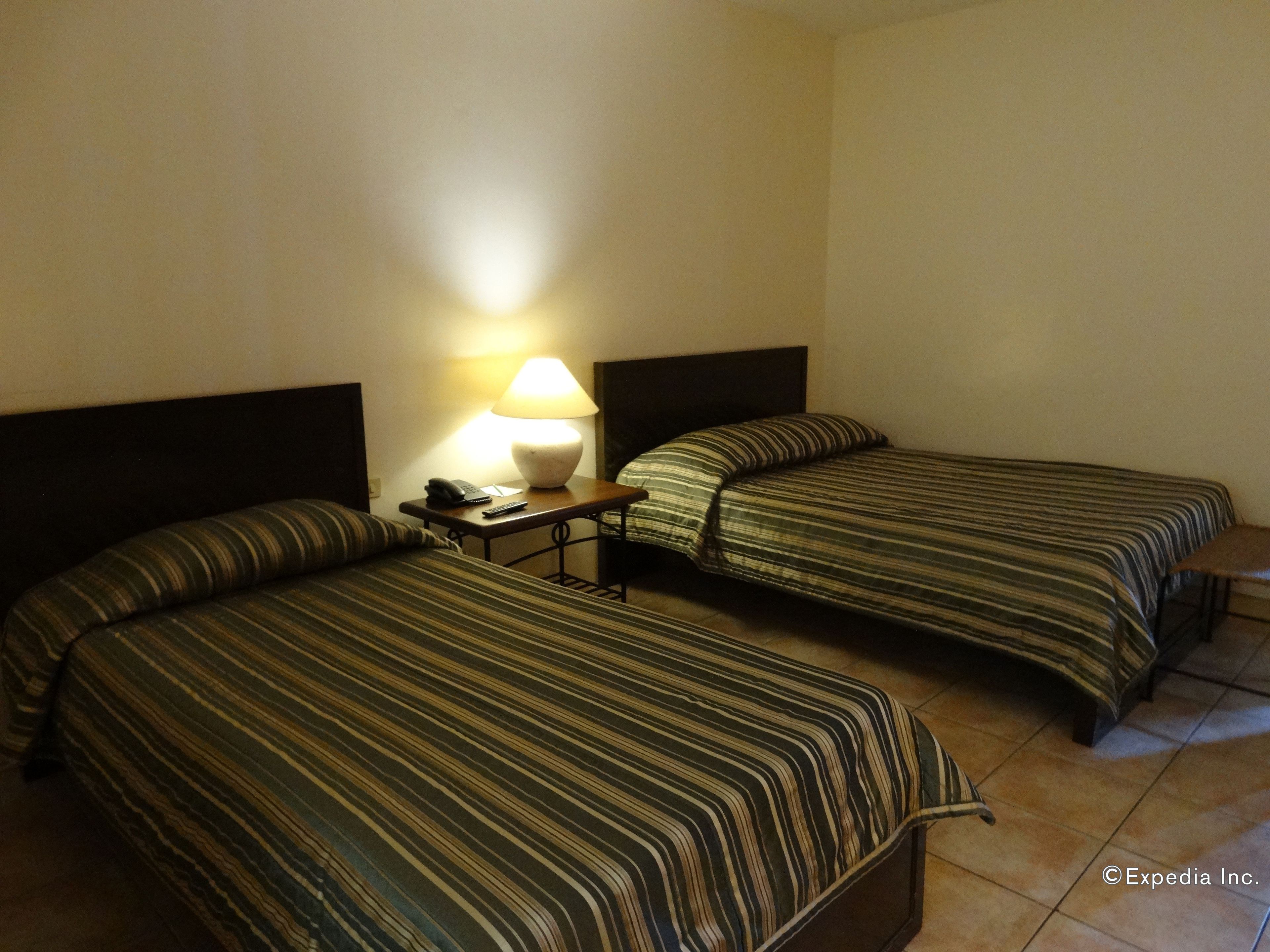 Habitación de hotel con dos camas, cada una con ropa de cama a rayas, una mesita de noche con lámpara y teléfono.