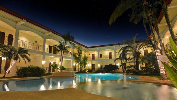 A hotel with a pool, multiple balconies, and palm trees.