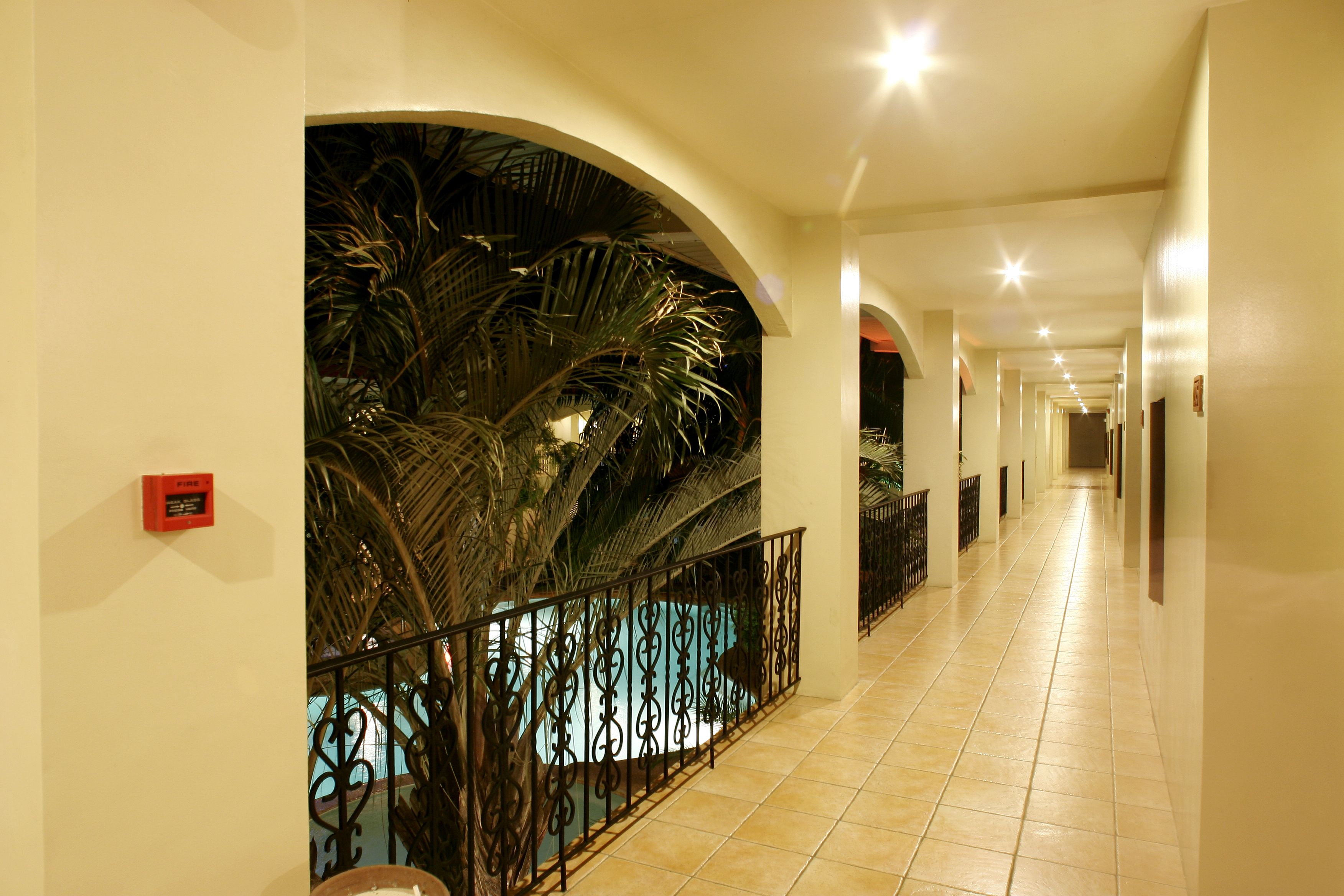 A hotel corridor with a pool area, featuring a tiled floor, arched ceilings, and a railing around the pool.