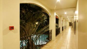 A hotel corridor with a pool area, featuring a tiled floor, arched ceilings, and a railing around the pool.