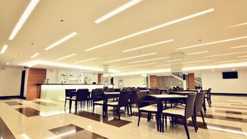 A modern dining area with long tables and chairs, a bar, and a staircase.