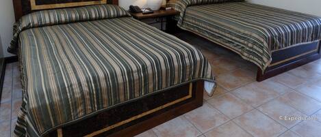 A hotel room with two beds, each with a wooden headboard and striped bedding. There is a nightstand with a lamp and a phone.