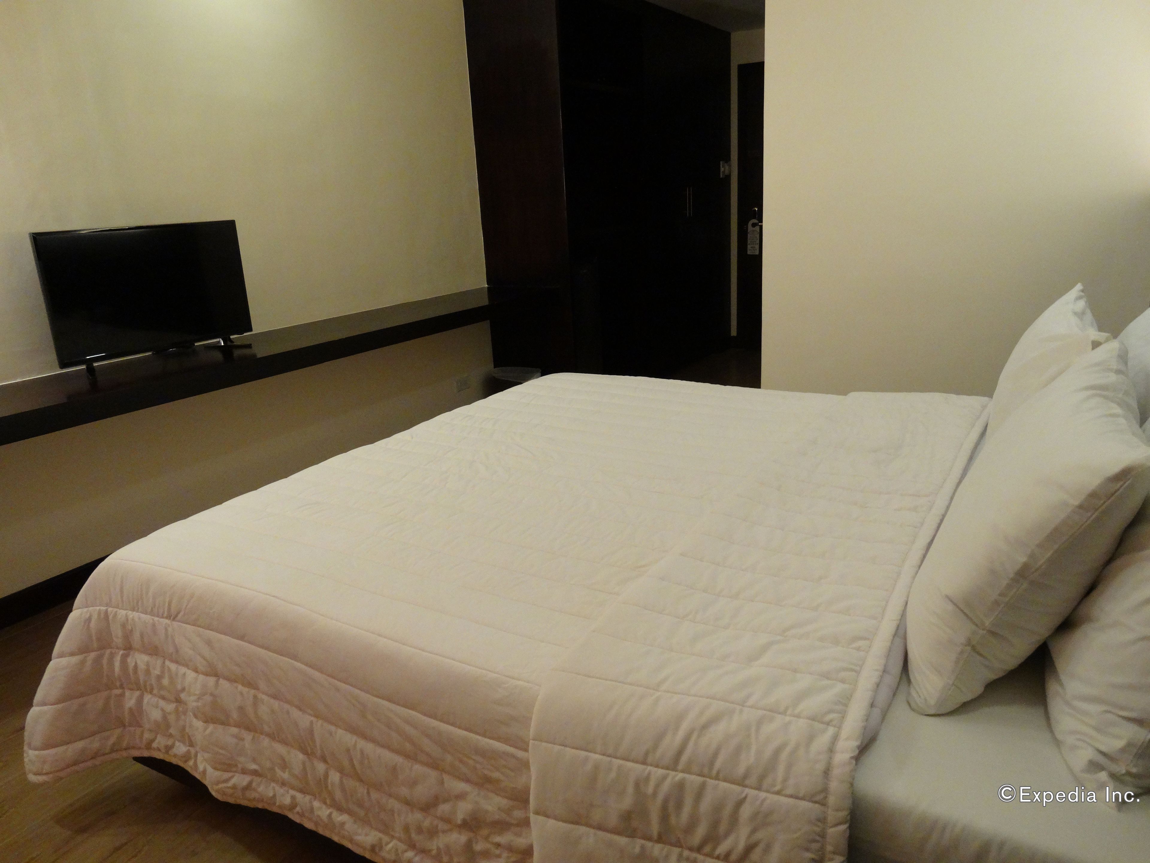 Une chambre d’hôtel avec un lit, un téléviseur à écran plat posé sur un meuble et une porte donnant sur une autre pièce.
