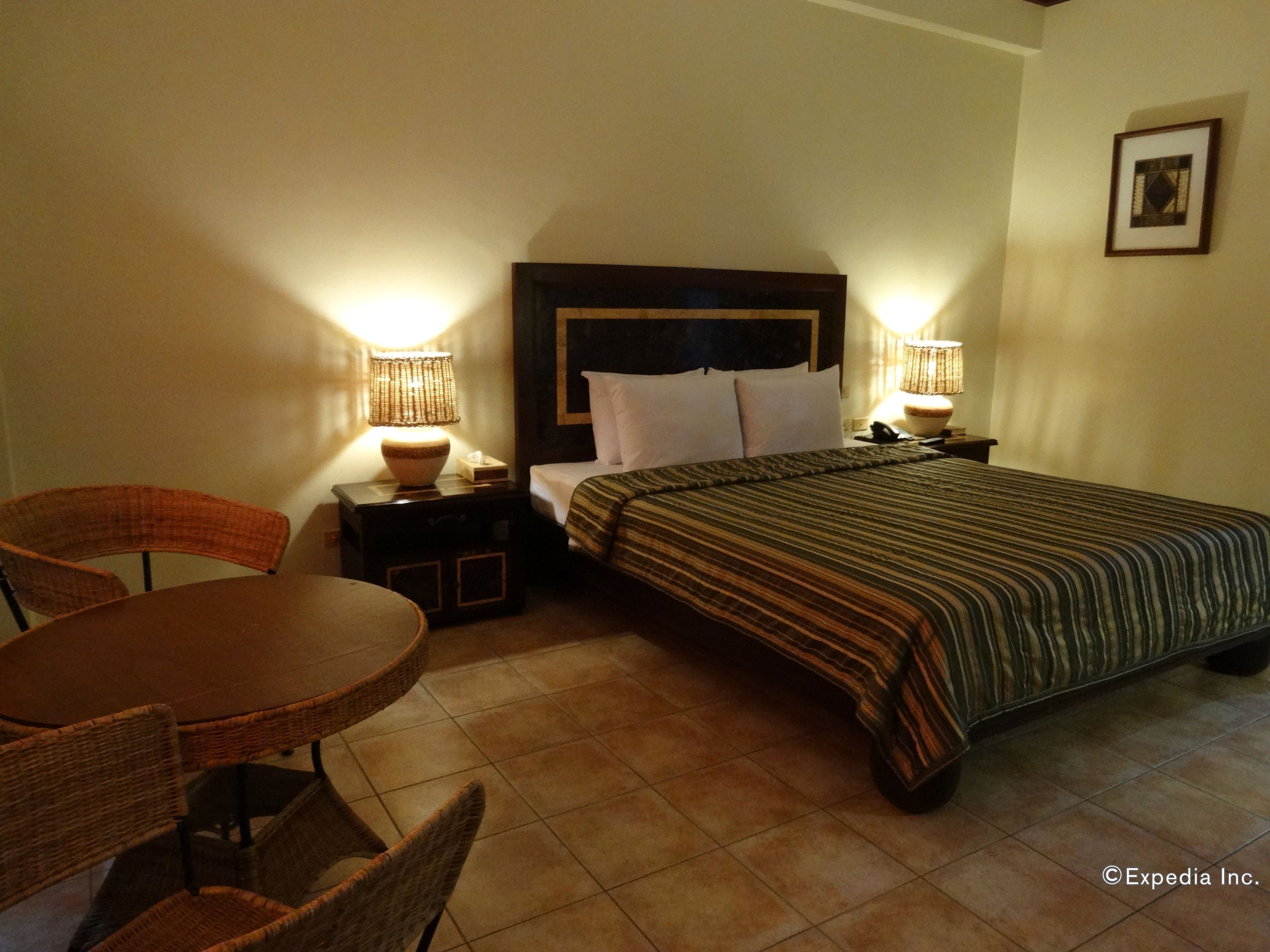 A hotel room with a bed, two bedside lamps, a small table with chairs, and a framed picture on the wall.