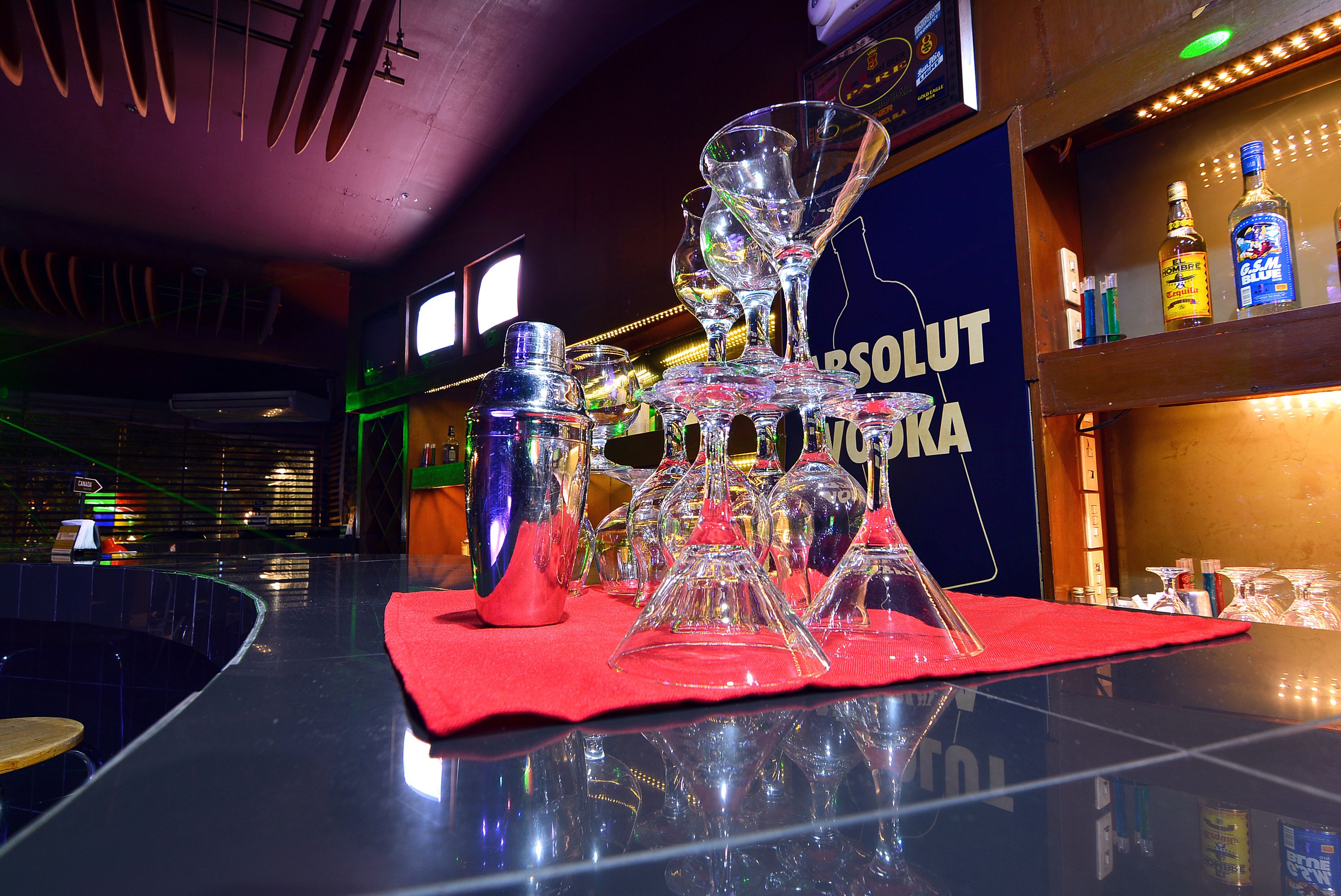 Een bar met een rode mat, divers glaswerk en flessen drank.