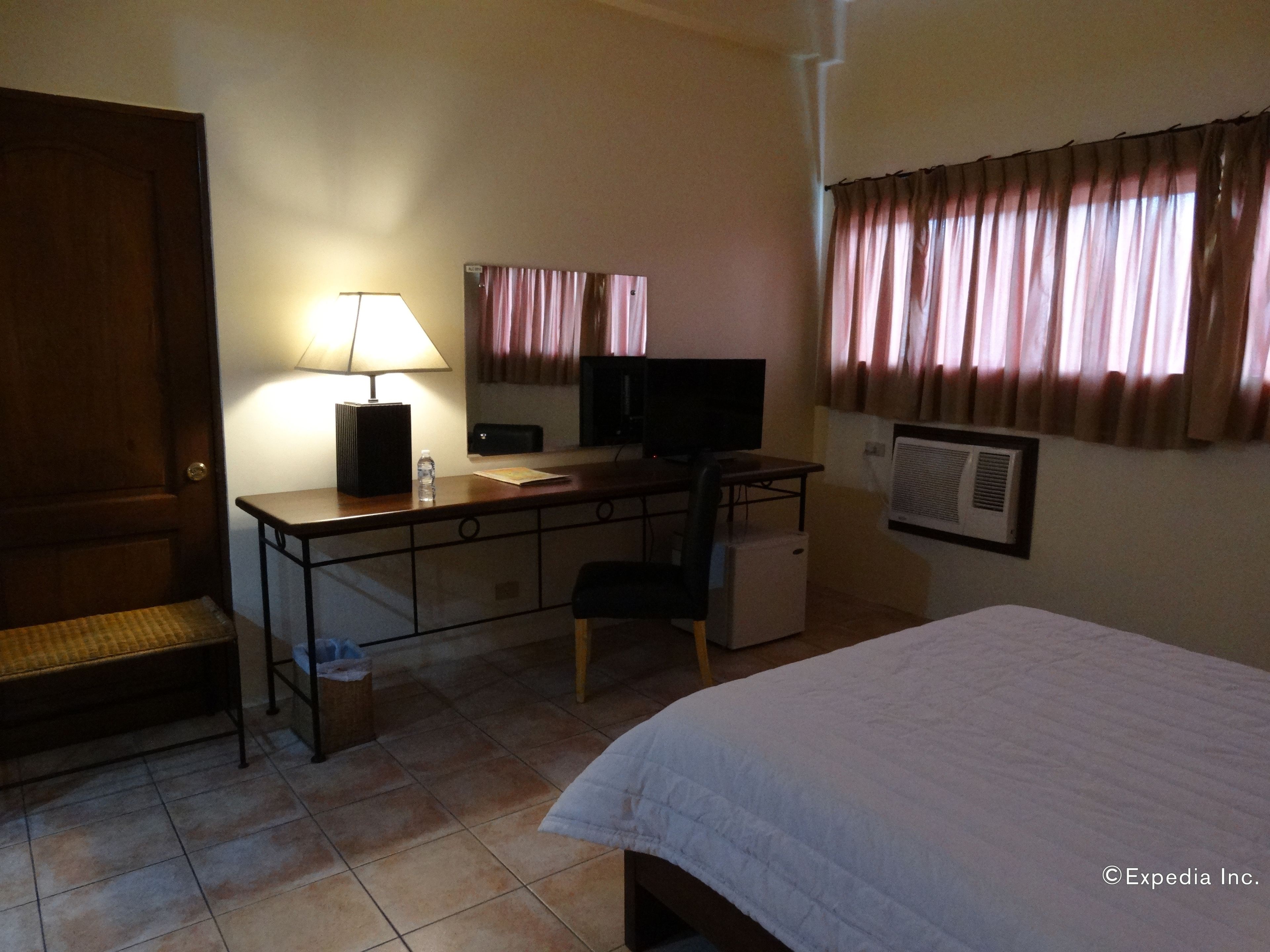 Una camera d'albergo con un letto, una scrivania, una sedia, una lampada, televisione e condizionatore d'aria.