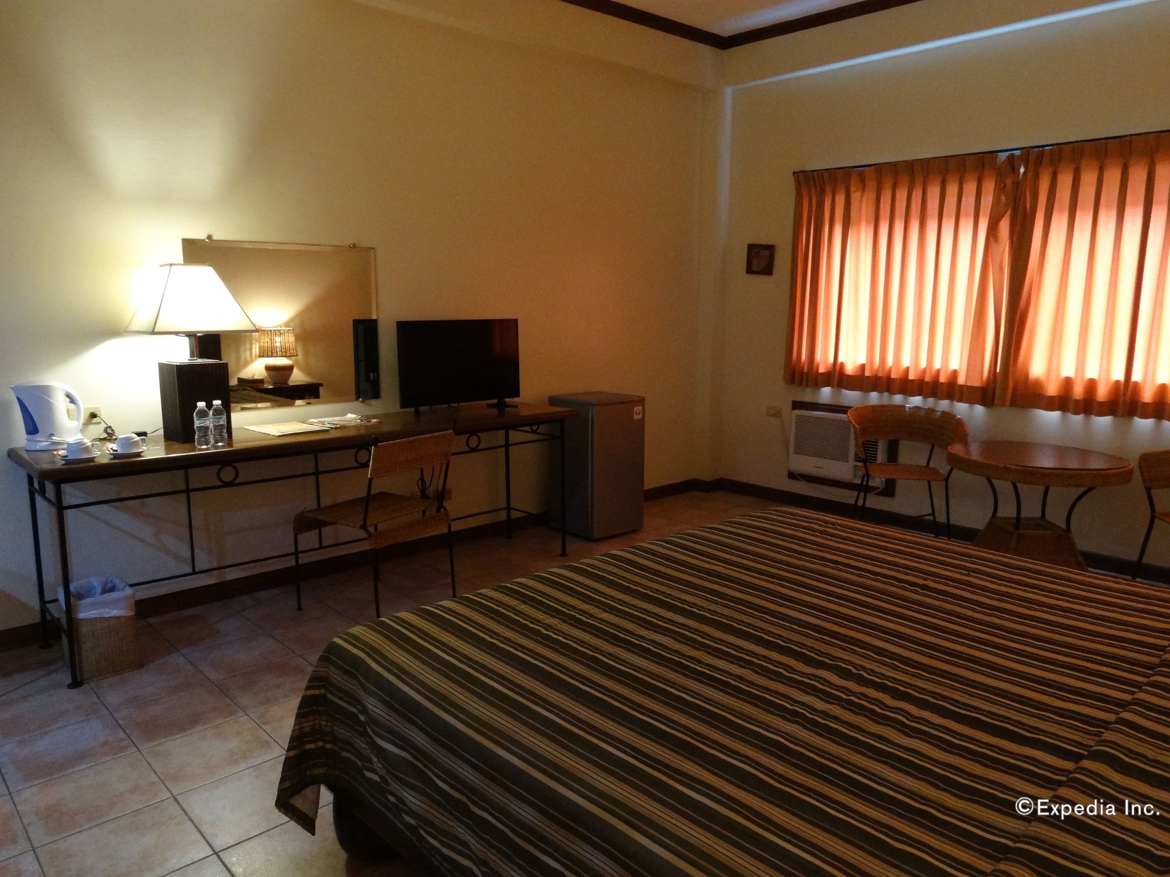A hotel room with a bed, desk, chair, TV, and a small table with chairs.
