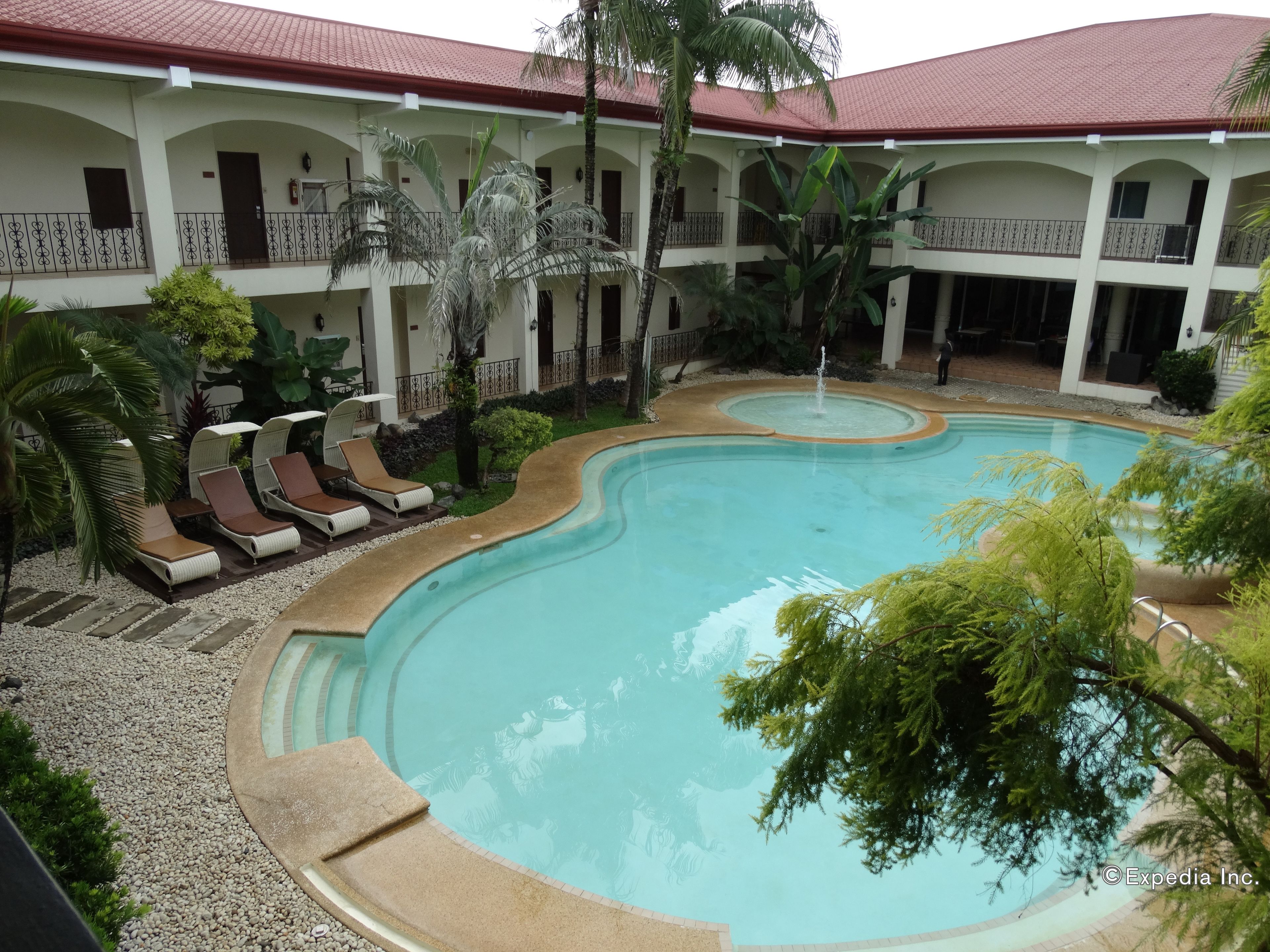 A pool area with lounge chairs, a fountain, and a building with balconies.