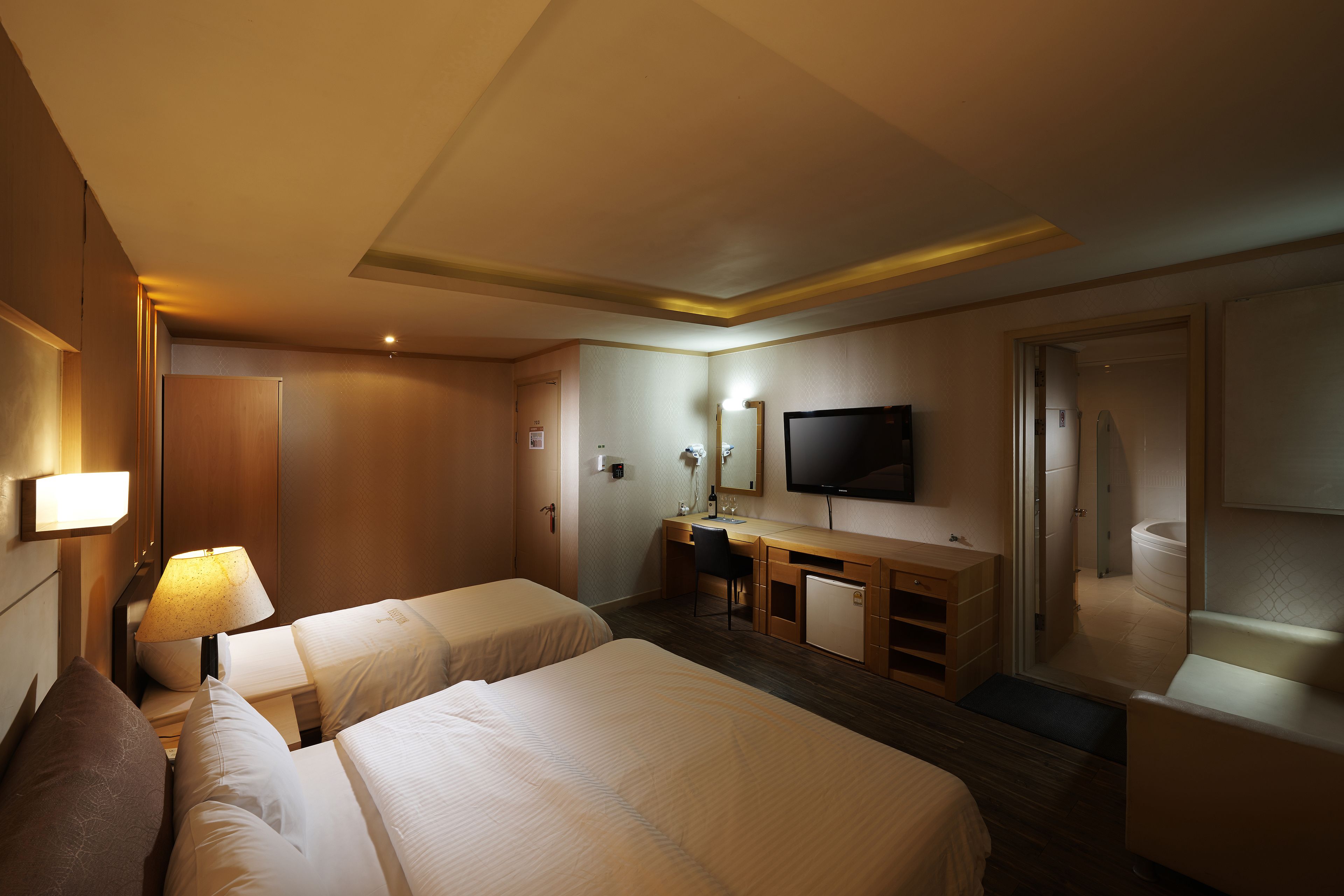 A hotel room with two beds, a desk, a television, and a bathroom.