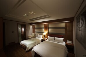 A hotel room with two beds, a desk, a chair, and a nightstand with a lamp. - Benikea Hotel Noblesse (Seoul)