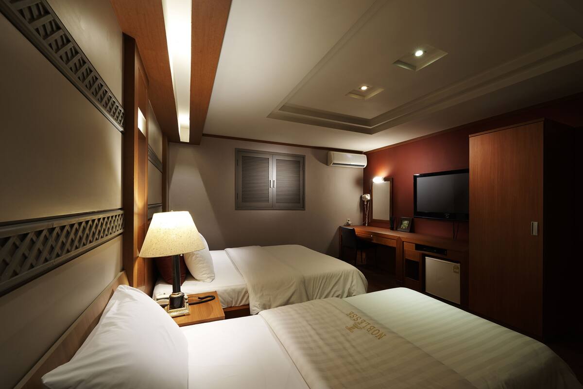 Habitación de hotel con dos camas, un escritorio con silla, televisión y aire acondicionado.