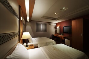 Habitación de hotel con dos camas, un escritorio con silla, televisión y aire acondicionado.