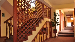A wooden staircase with a lattice design, a door labeled 'SALIDA', and a potted plant on the landing. - Hotel Vilandré (Cusco)