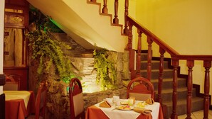 A dining area with a stone wall, wooden staircase, and tables set for breakfast. - Hotel Vilandré (Cusco)