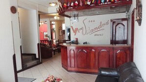 A reception area with a wooden counter, a black leather sofa, and a floral centerpiece on a table. - Hotel Vilandré (Cusco)