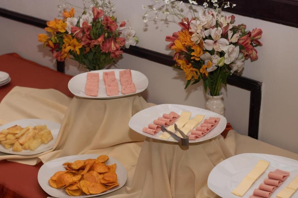 Ett buffébord med fat fulla av skivad kött, ost och potatischips, omgivet av blomsterarrangemang.