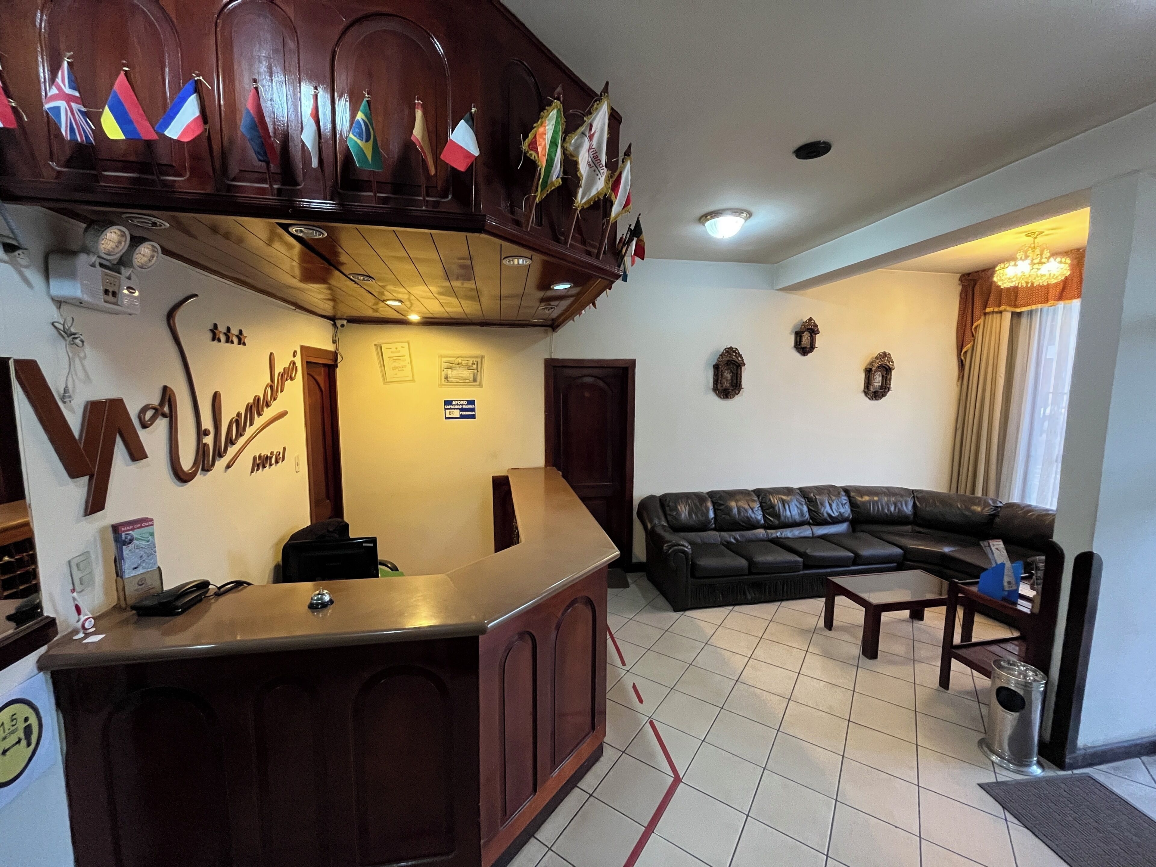 A reception area with a wooden counter, a black leather sofa, and a chandelier. Flags are displayed on the wall above the counter.