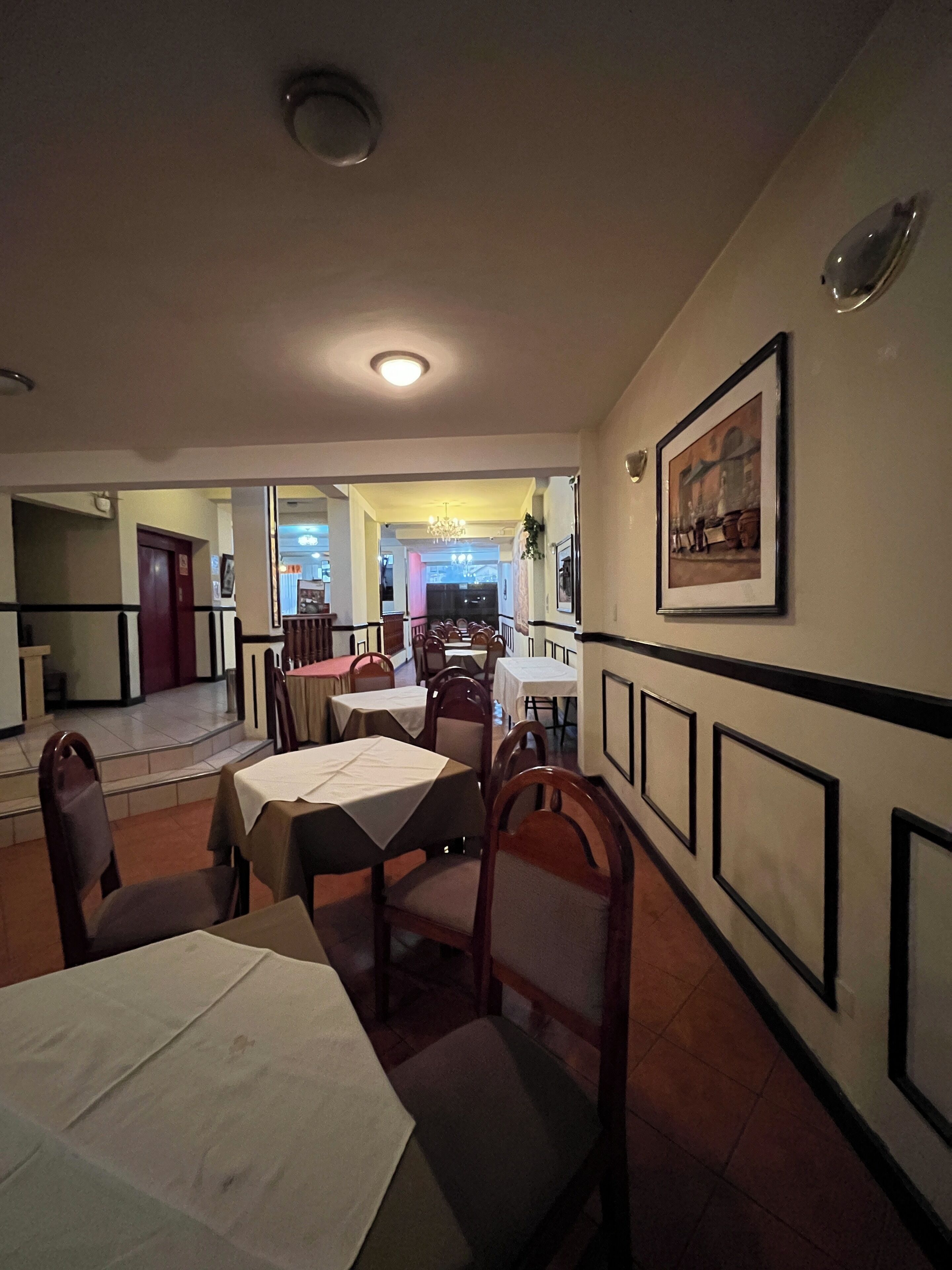 A dining area with tables and chairs, a chandelier, and a framed picture on the wall.
