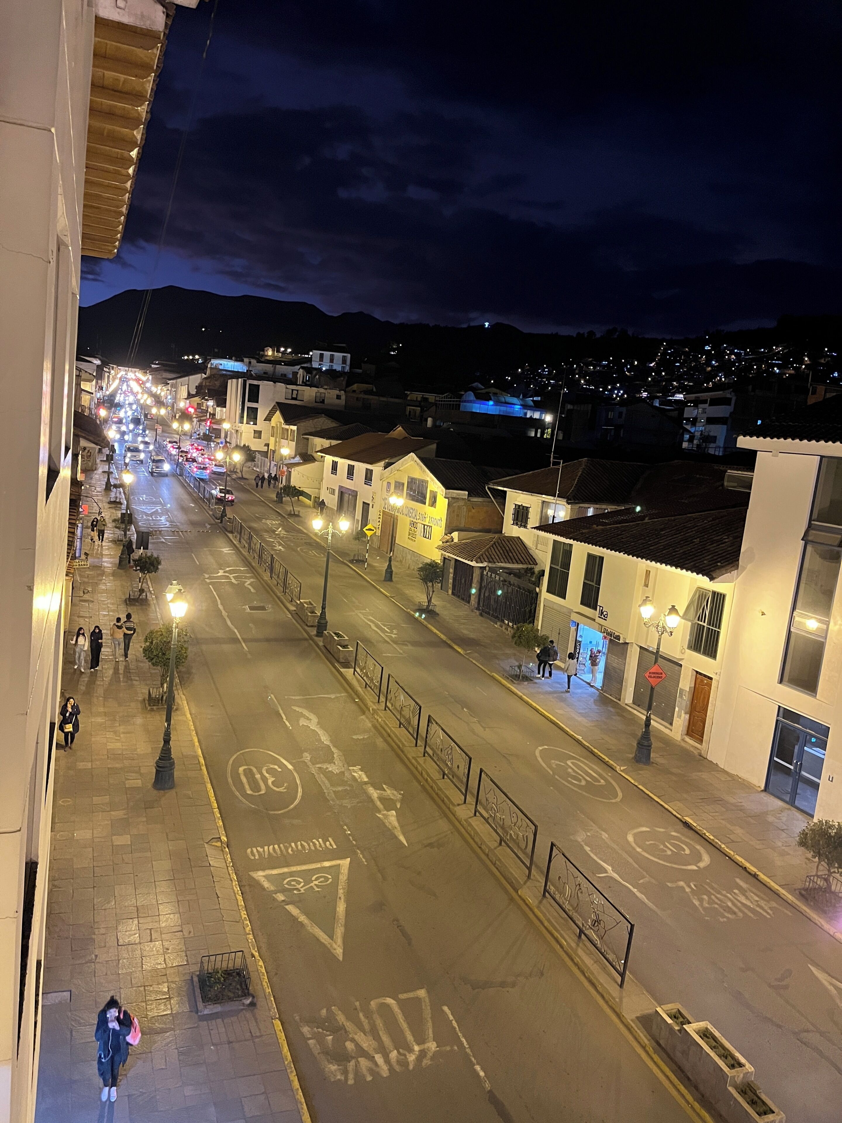 A nighttime street view with buildings, a road with traffic, and street lamps.