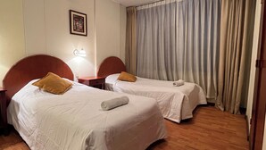 A hotel room with two beds, a nightstand, a lamp, a framed picture on the wall, and a window with curtains. - Hotel Vilandré (Cusco)