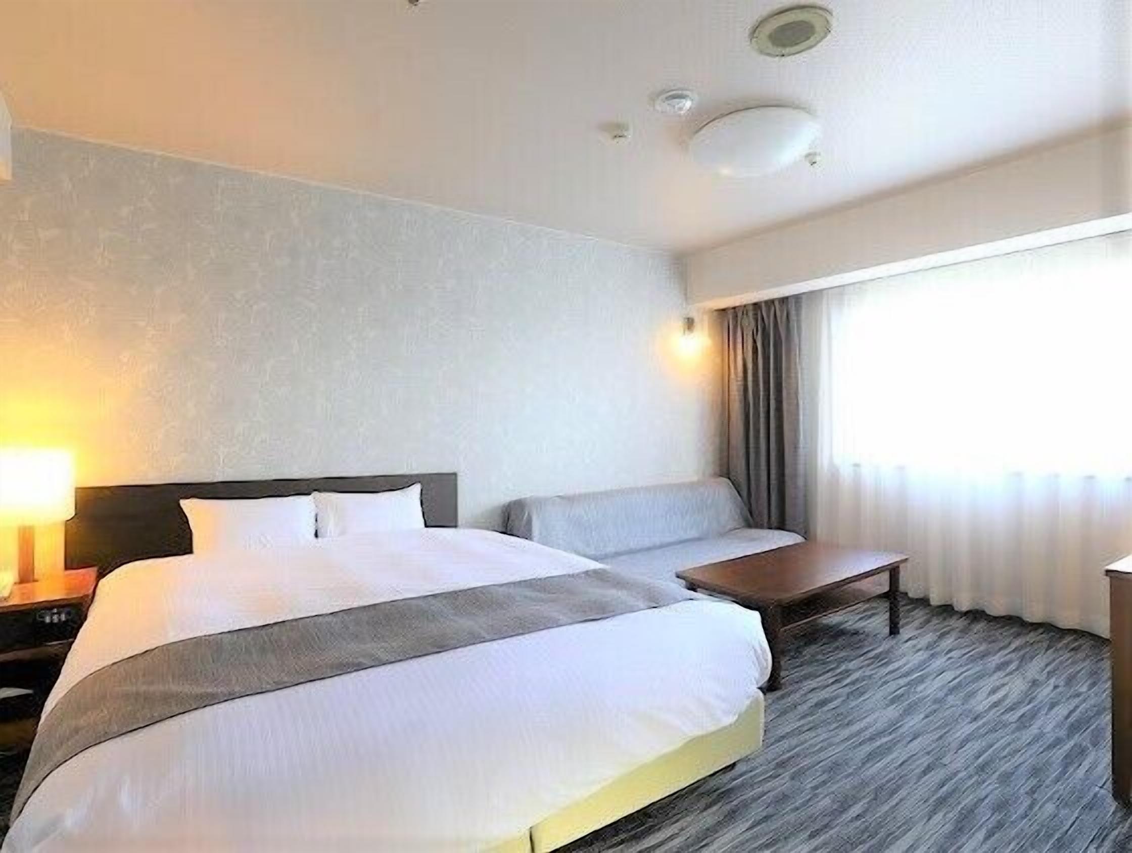 A hotel room with a large bed, bedside tables, a seating area, and a window with curtains.