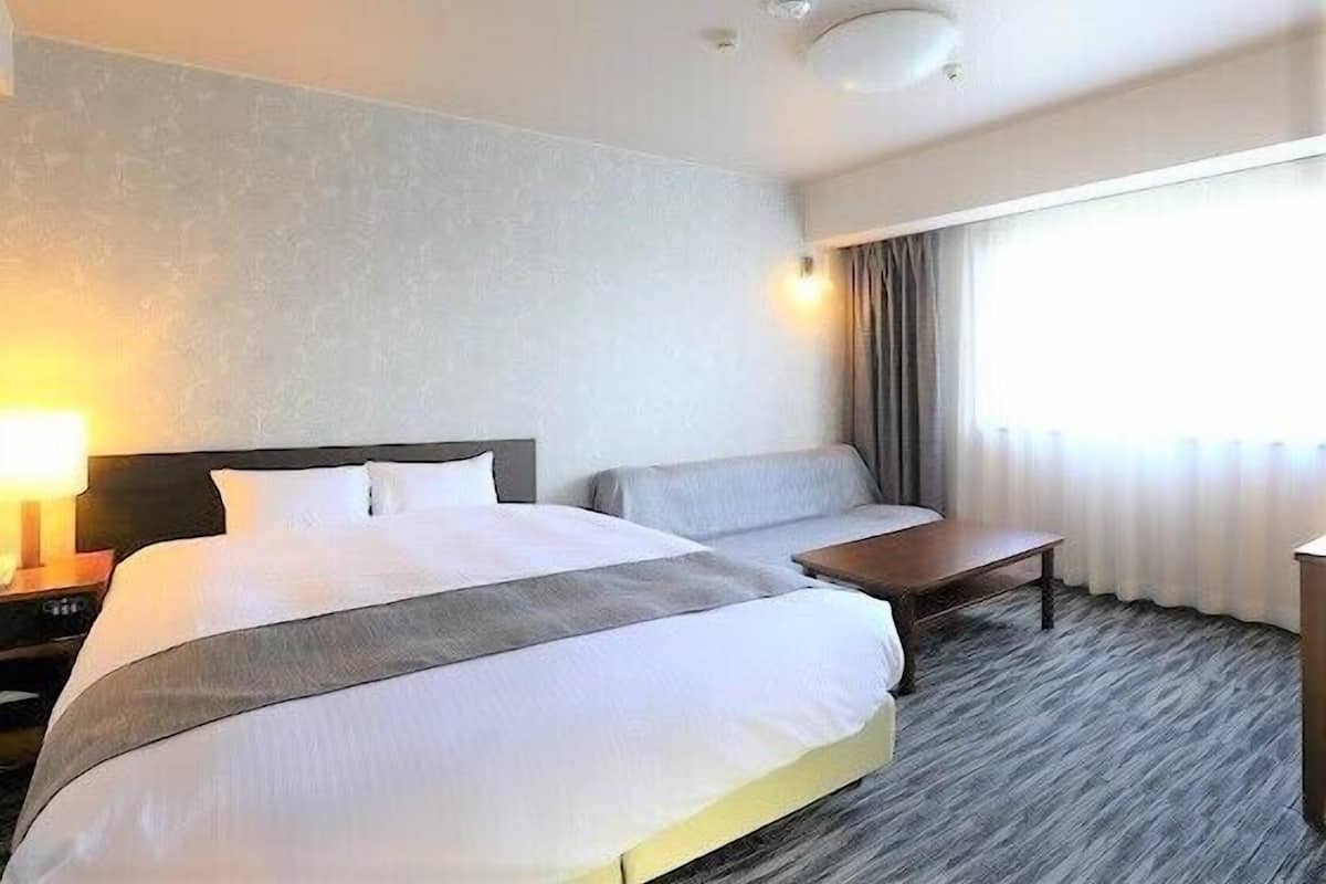 A hotel room with a large bed, bedside tables, a seating area, and a window with curtains.