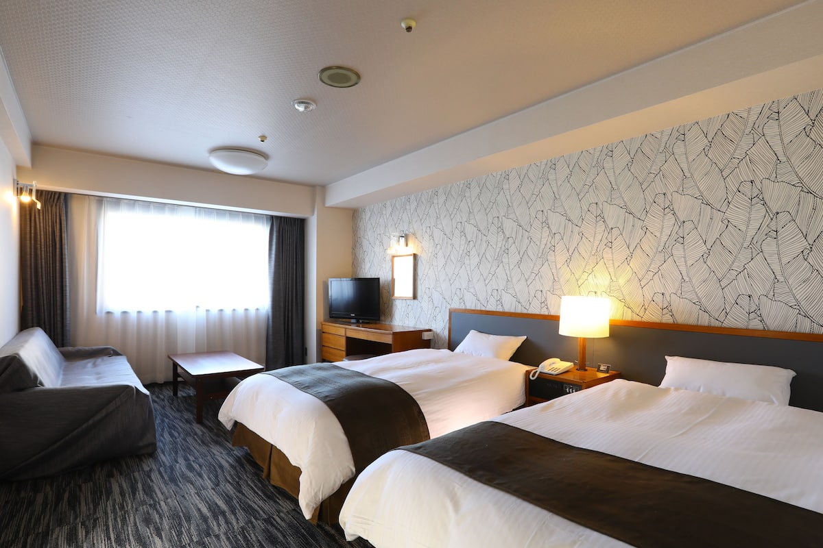 Une chambre d’hôtel avec deux lits, un bureau, une télévision et un papier peint à motifs.