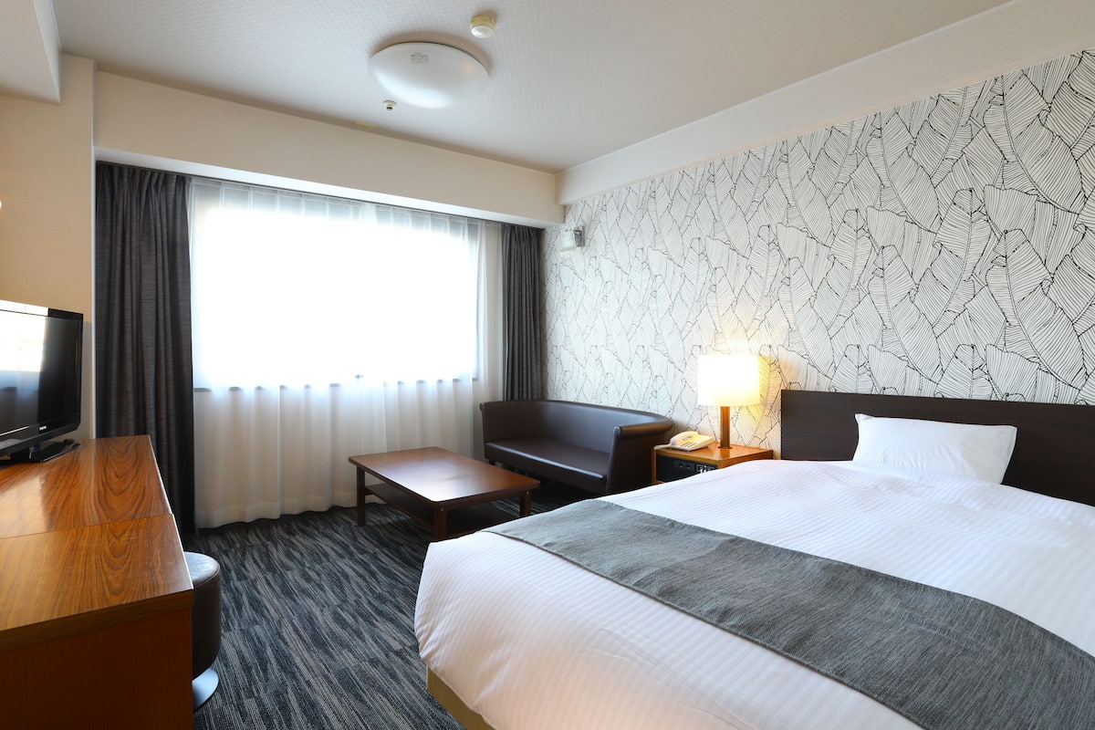 Une chambre d’hôtel avec un lit, un bureau, une chaise, une télévision et une fenêtre avec des rideaux.