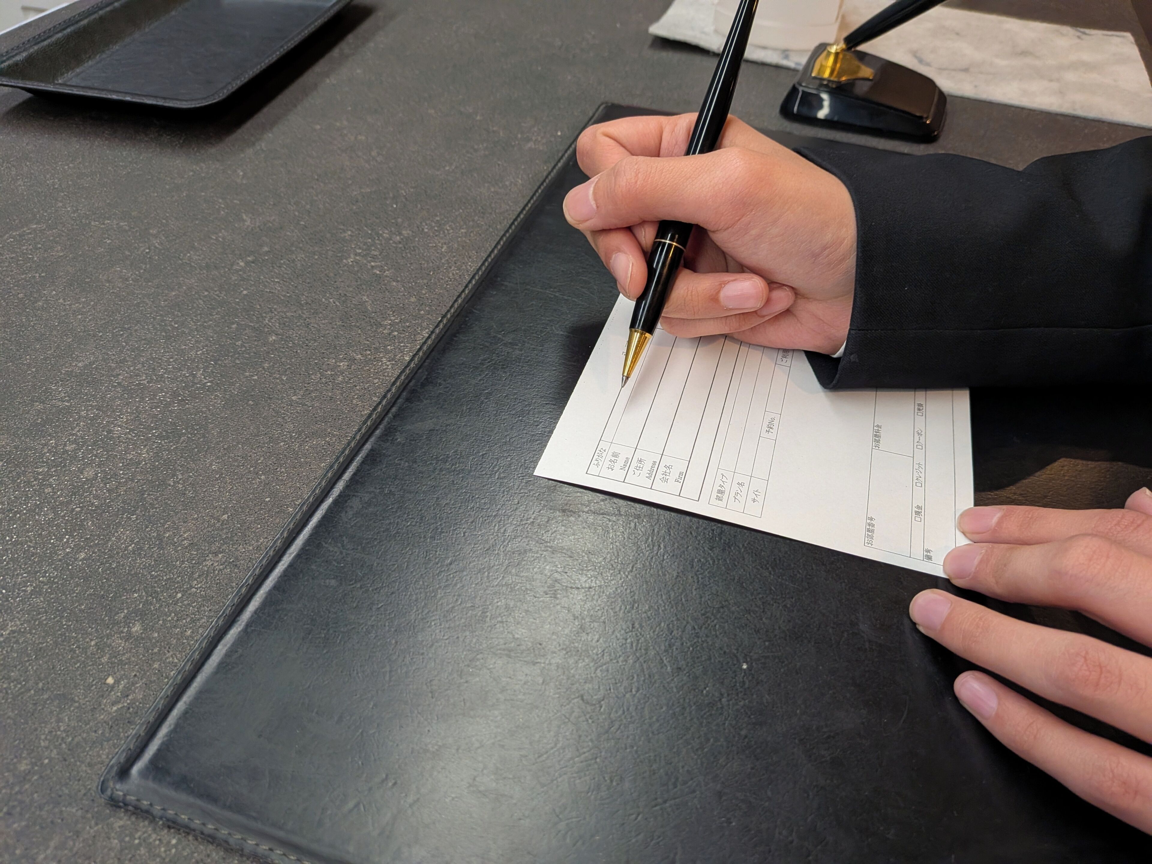 A person signing a document on a dark, matte surface.