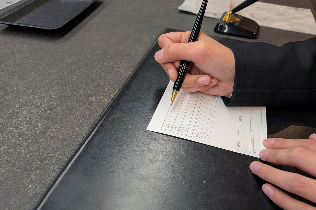 Une personne signant un document sur une surface sombre et mate.