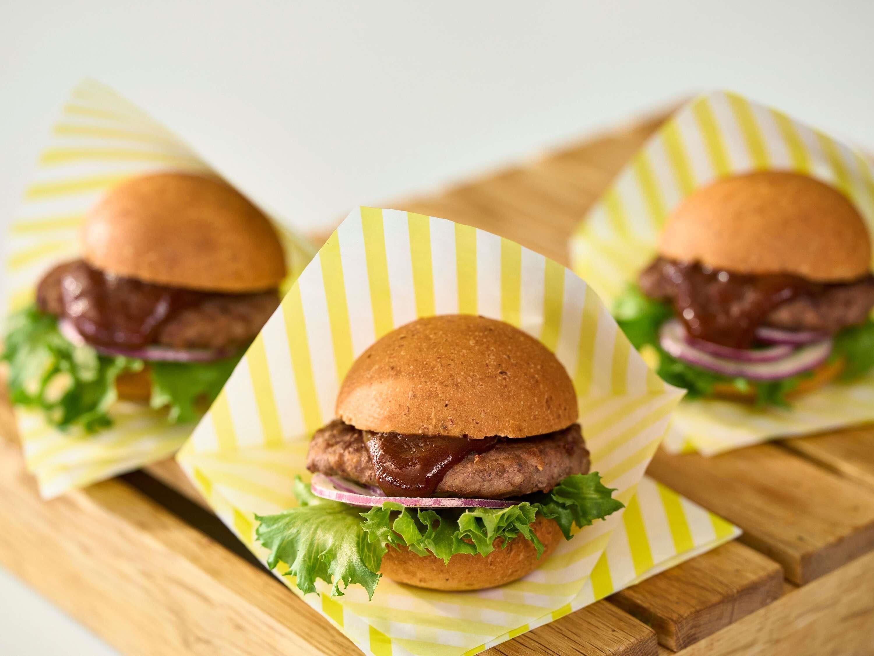 Three burgers on wooden boards with yellow and white striped paper liners.