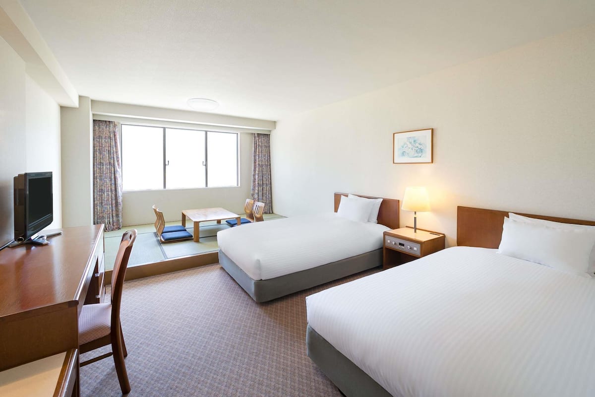 Une chambre d’hôtel avec deux lits, un bureau, une chaise, une télévision et une fenêtre avec des rideaux.