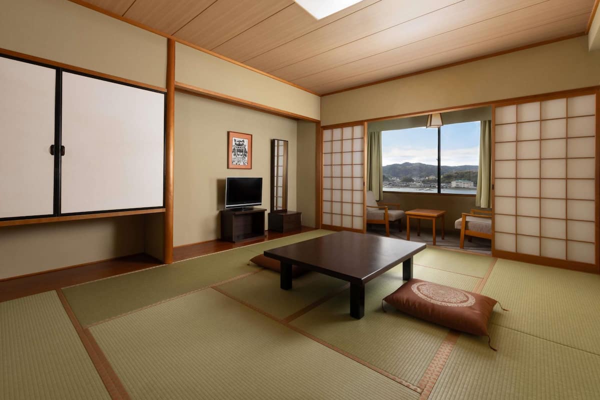 Une pièce de style japonais traditionnel, avec un sol recouvert de tatamis, une table basse, un téléviseur et une vue sur les montagnes.