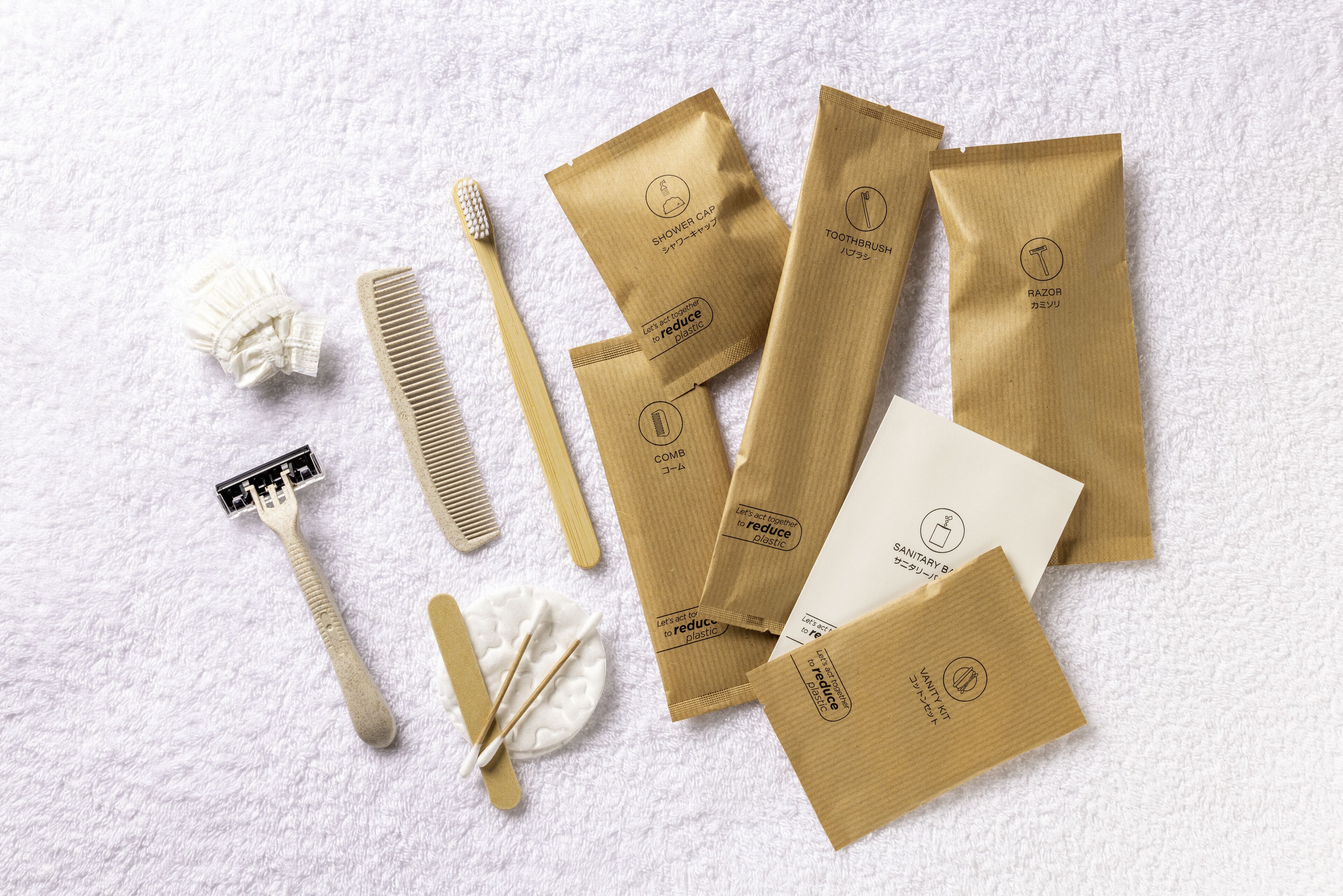 Variedad de artículos de tocador, incluyendo peine, cepillo de dientes, maquinilla de afeitar y cepillo para el cabello, junto con varias bolsas de papel marrón con logotipos y texto.
