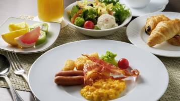 A breakfast setting with plates of eggs, bacon, sausages, and a fruit plate.