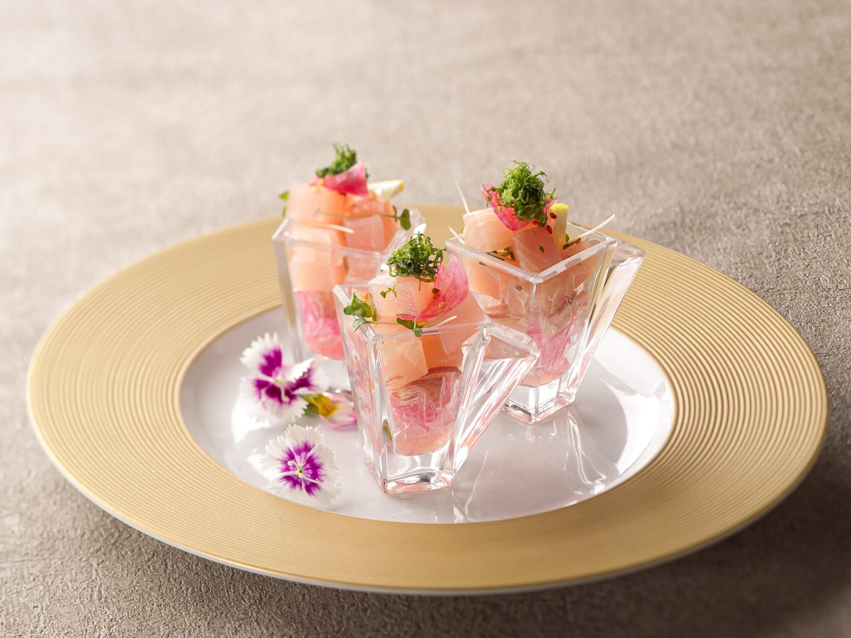 Three glass cubes with pink and white contents, garnished with green herbs, on a beige plate with a gold rim.