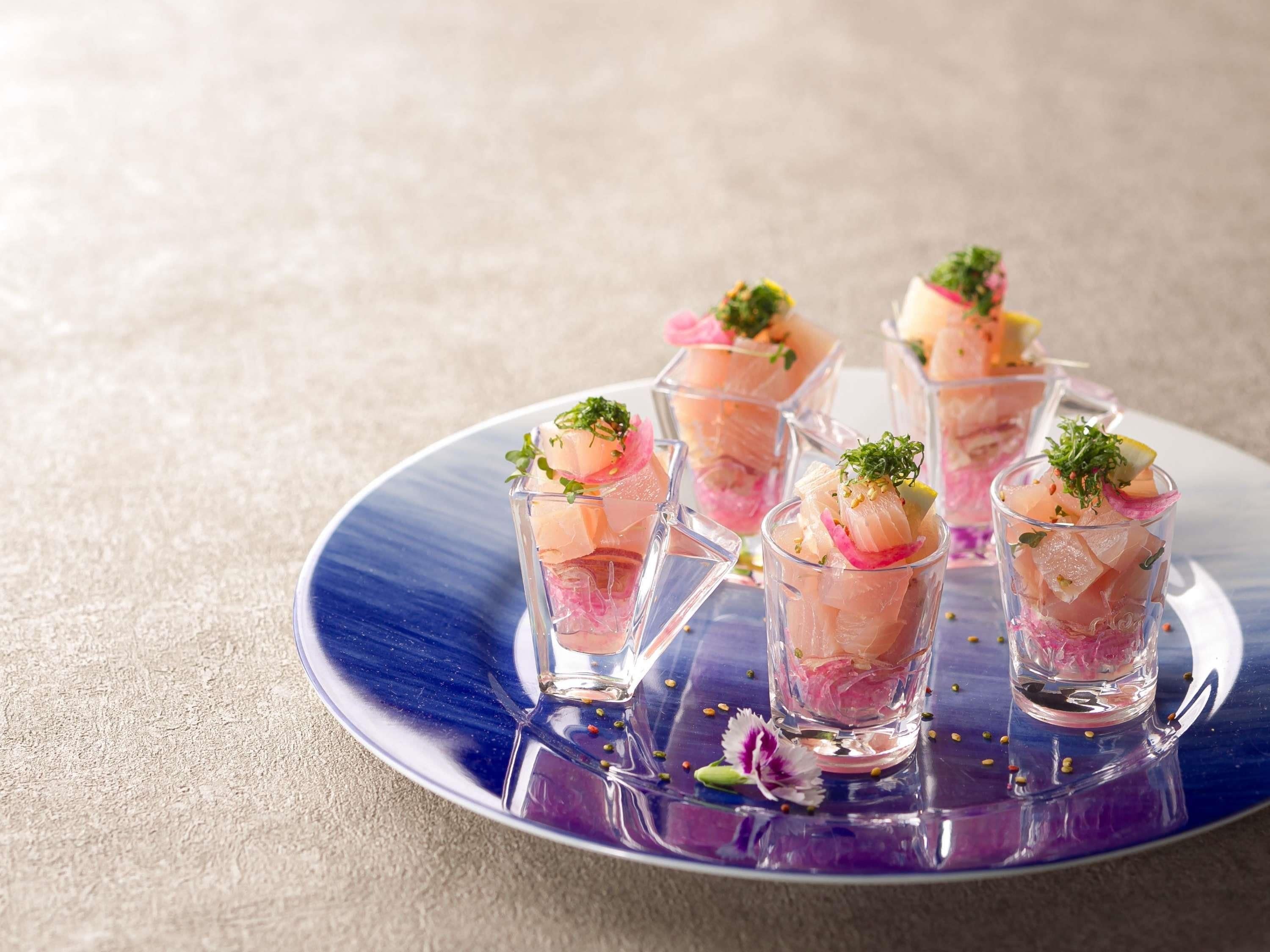 A blue plate with clear glasses containing a pinkish food item, garnished with green herbs and a flower.