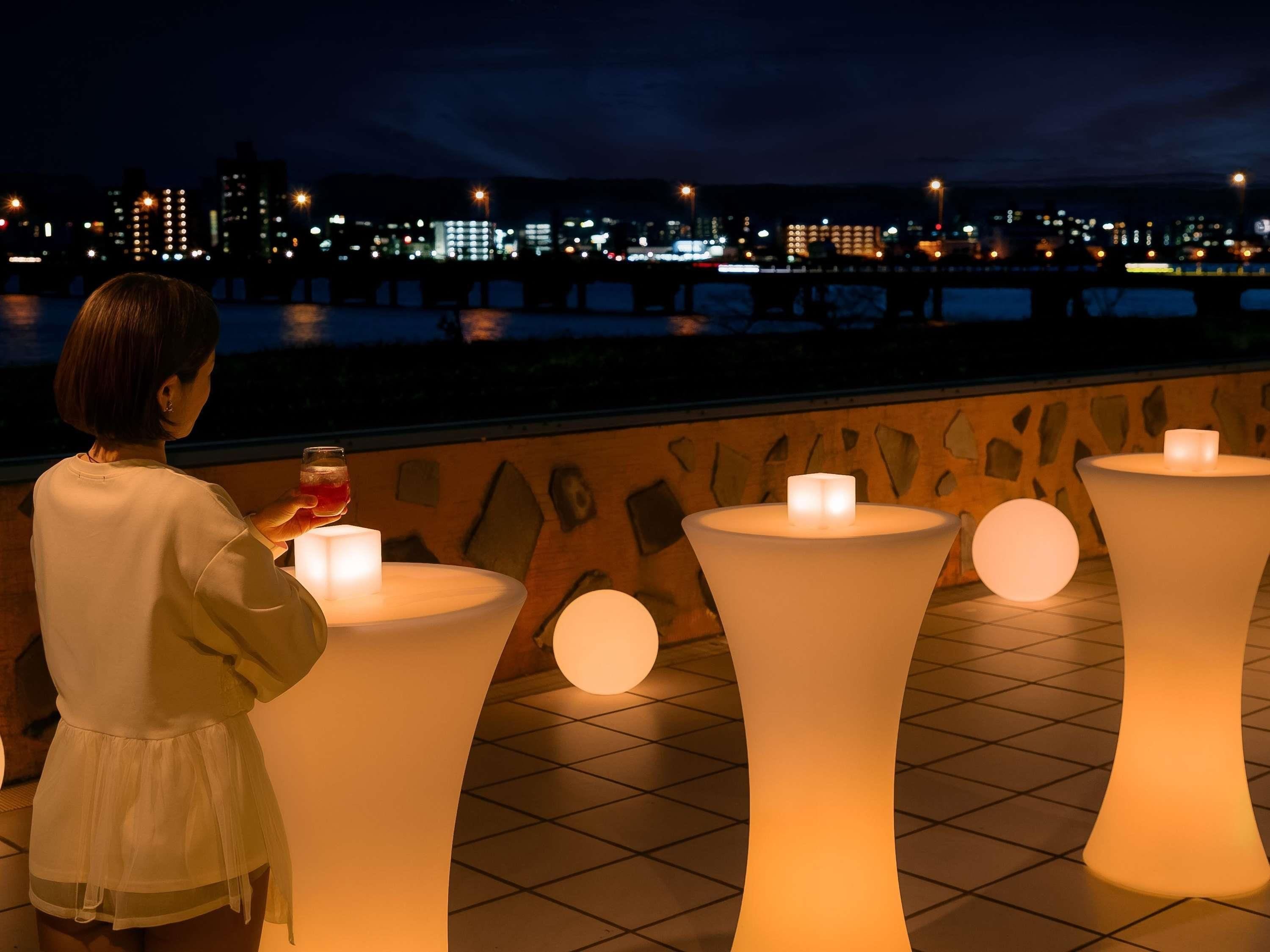 A person standing by a table with a lit candle, overlooking a cityscape at night.